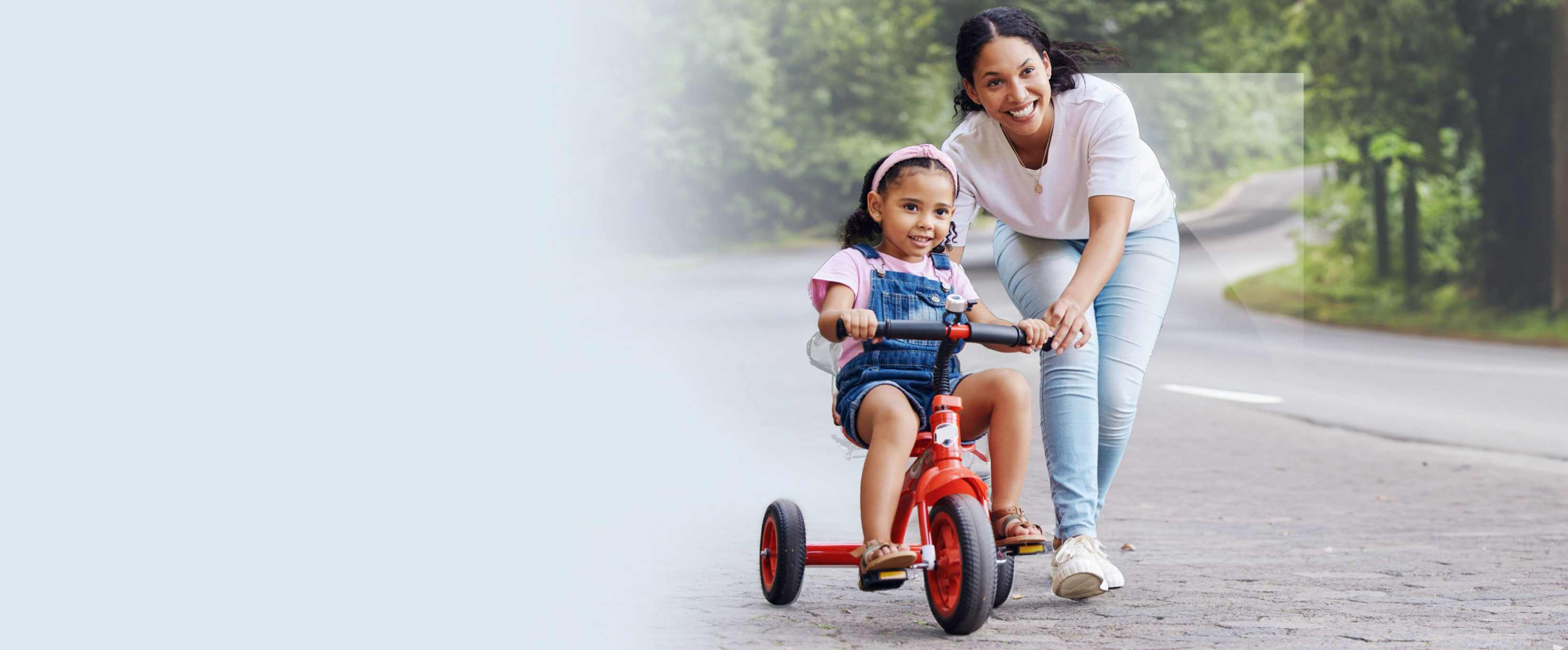 A happy scene of a woman pushing a young child on a tricycle outdoors.